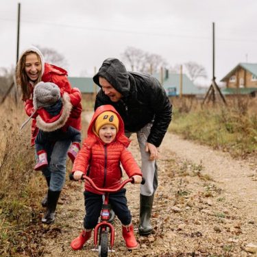 Happy family enjoying a rainy day outside with a bike ride and playful togetherness.